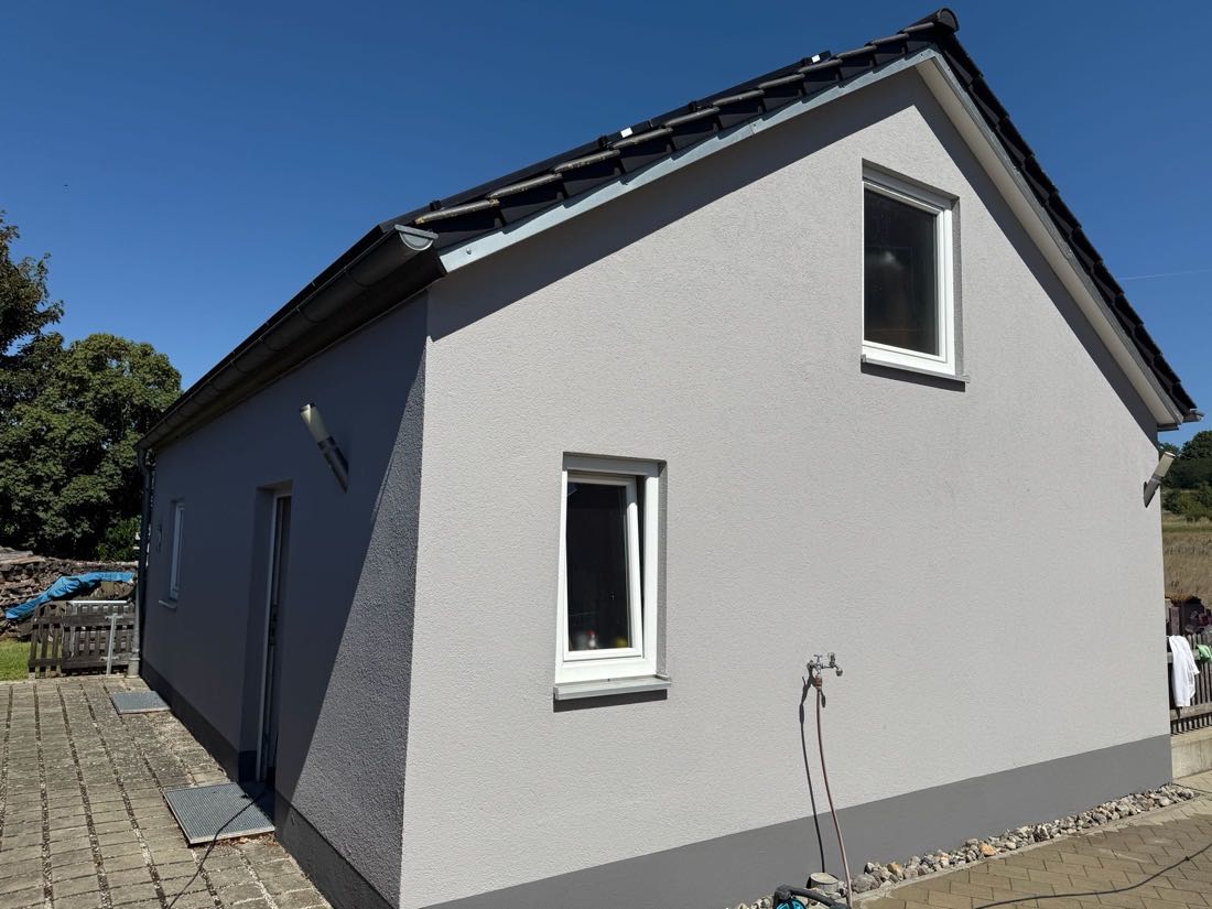 Anbau mit grauer Fassade, weißen Fenstern und dunklem Dach