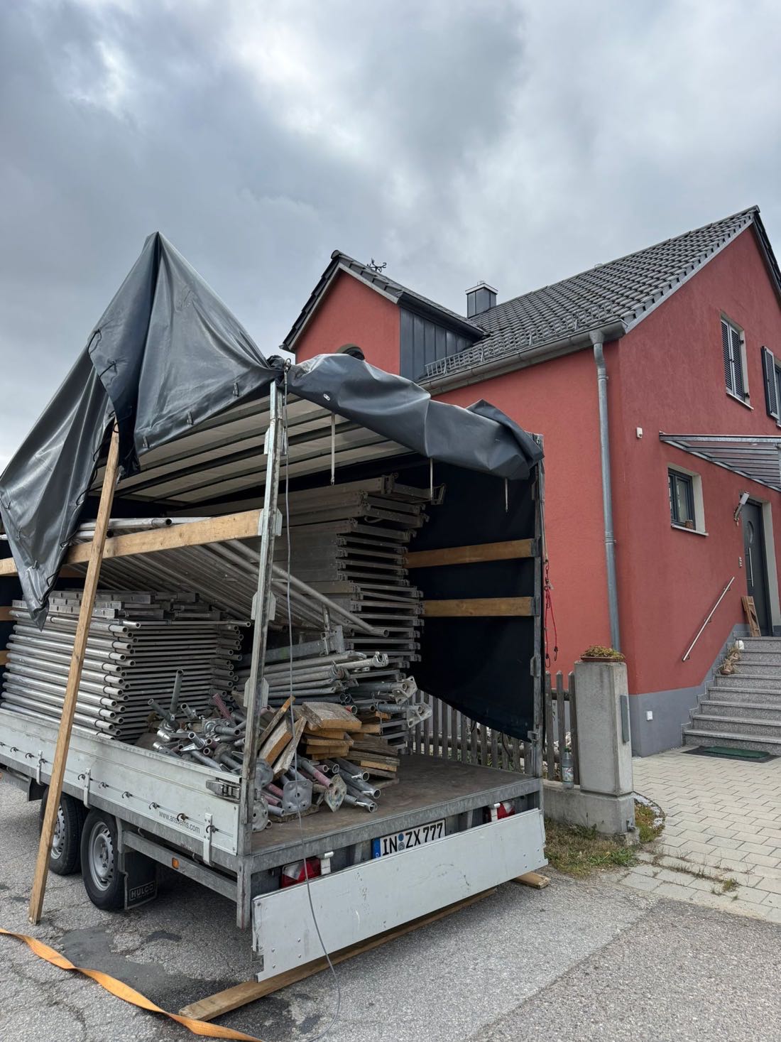 Gerüstanhänger vor einem fertig gestrichenen roten Wohnhaus