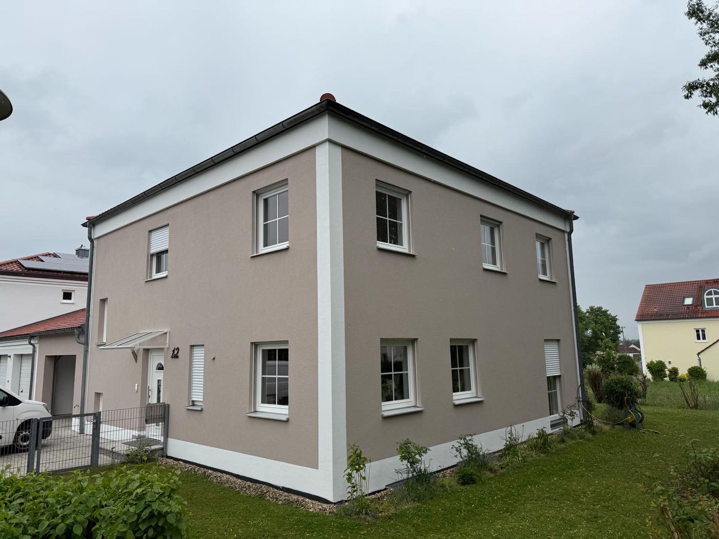 Wohnhaus mit neu gestrichener Fassade in warmem Greige und weißen Fensterfaschen