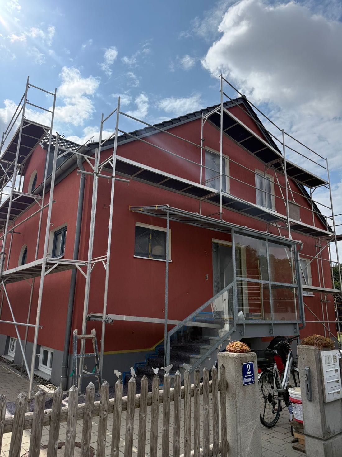 Eingerüstete Hausfassade während der Malerarbeiten mit frisch aufgetragenem rotem Anstrich