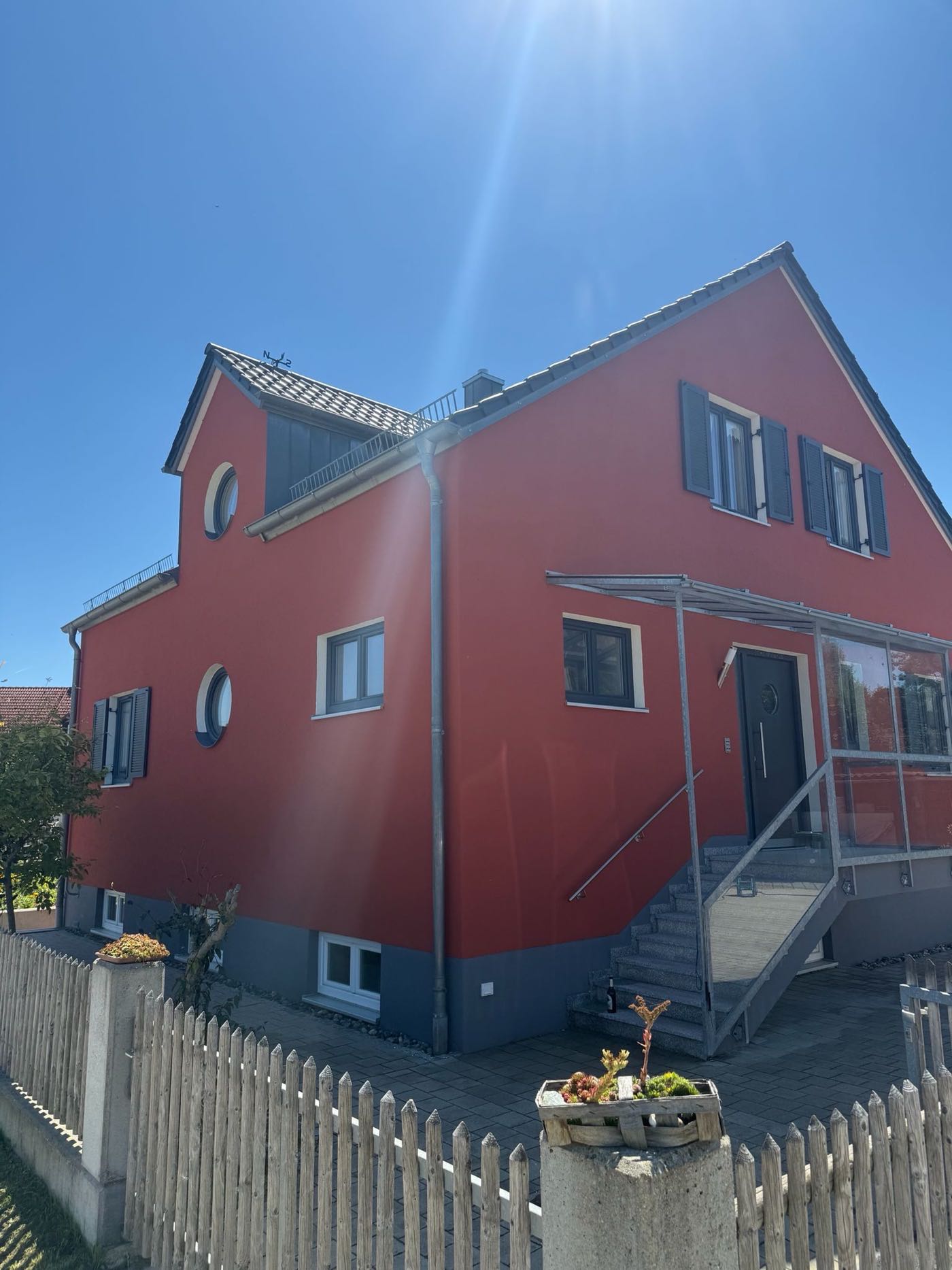 Wohnhaus mit rot gestrichener Fassade, anthrazitfarbenem Sockel und dunklen Fensterläden