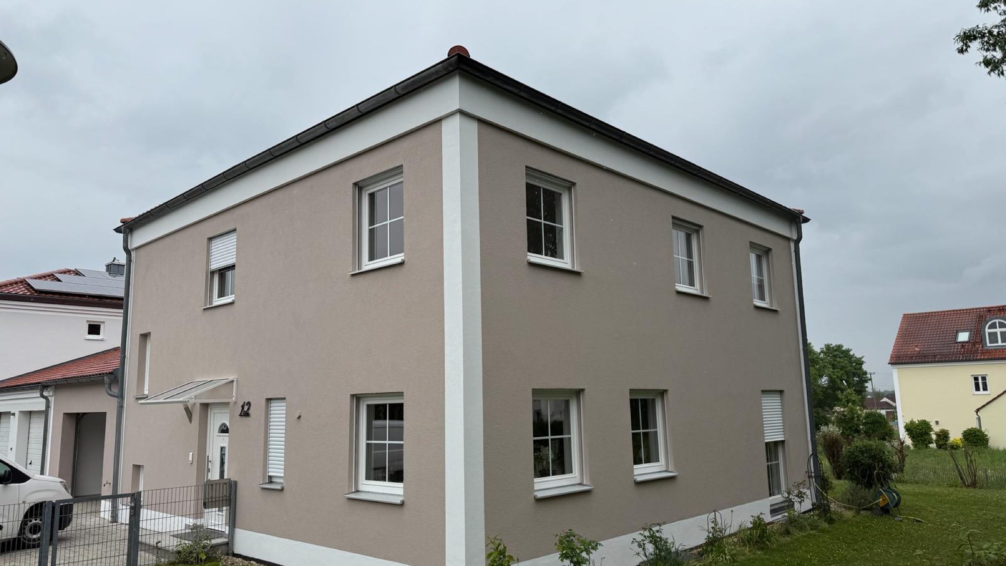 Einfamilienhaus mit neu gestrichener Fassade in warmem Greige und weiß abgesetzten Fensterfaschen
