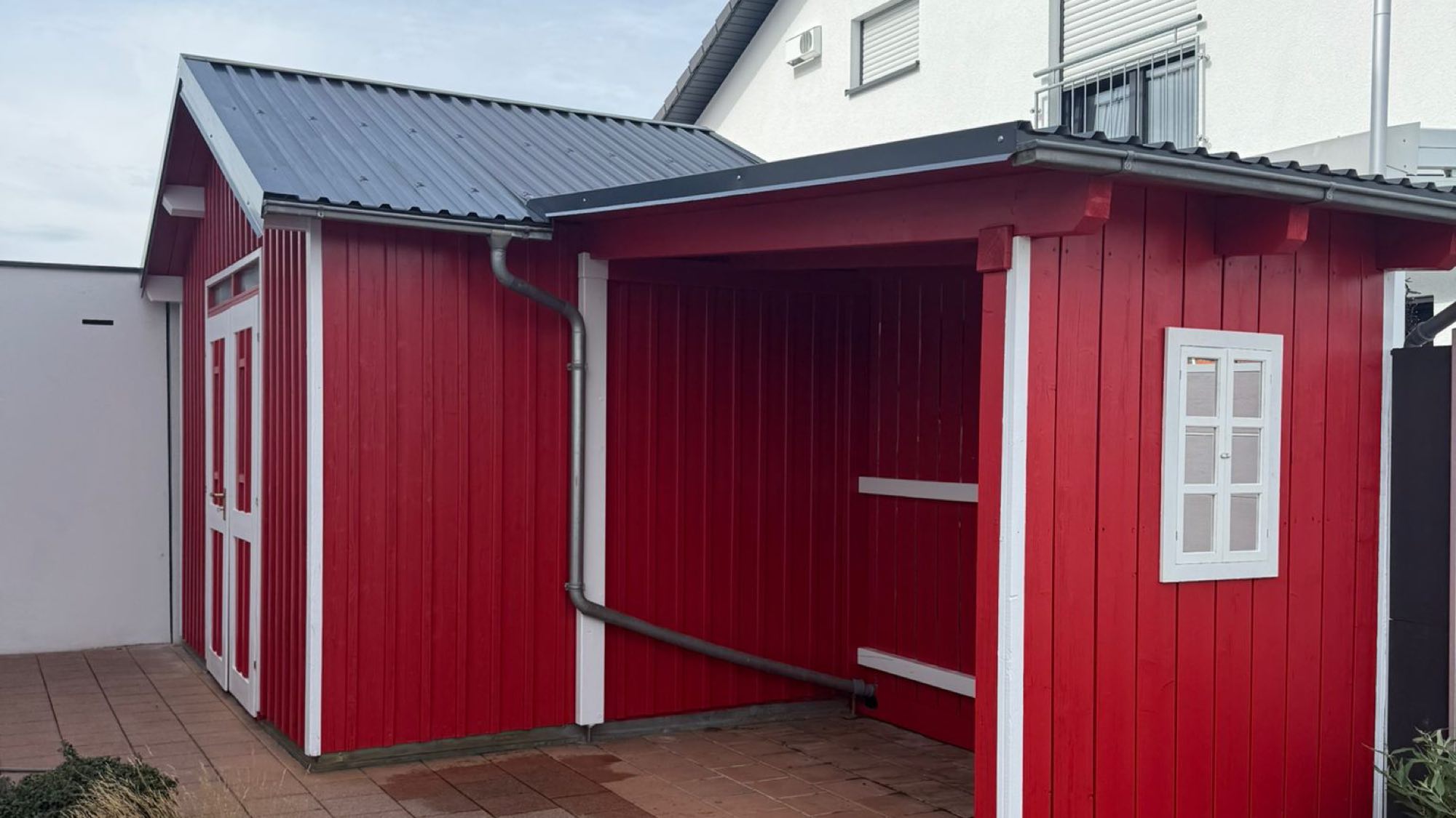Holzgebäude im Garten nach dem Neuanstrich in Rot mit weiß abgesetzten Leisten und Türrahmen