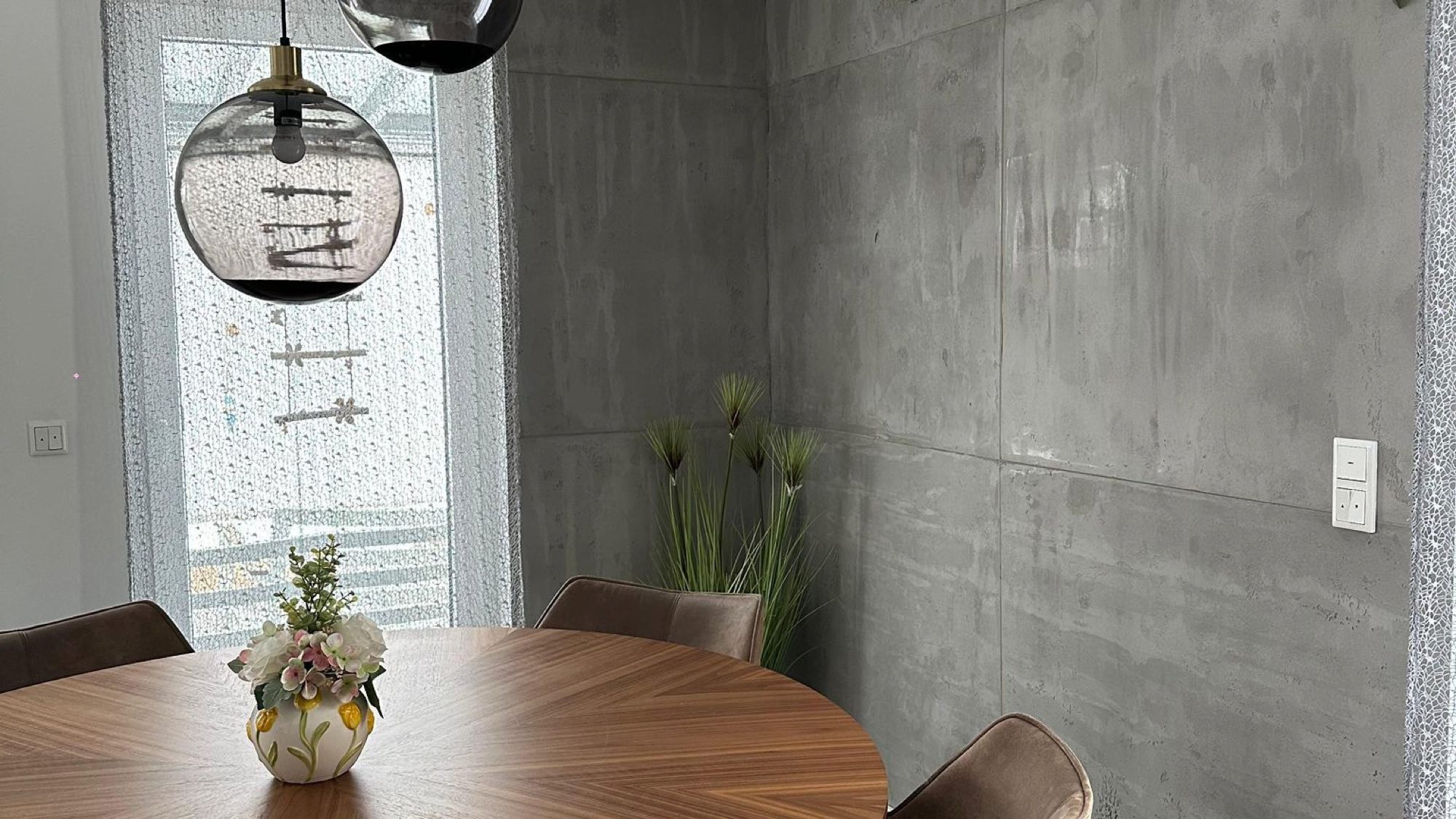 Essbereich mit einer in Sichtbeton-Optik gespachtelten Wand, Holztisch und Pendelleuchten