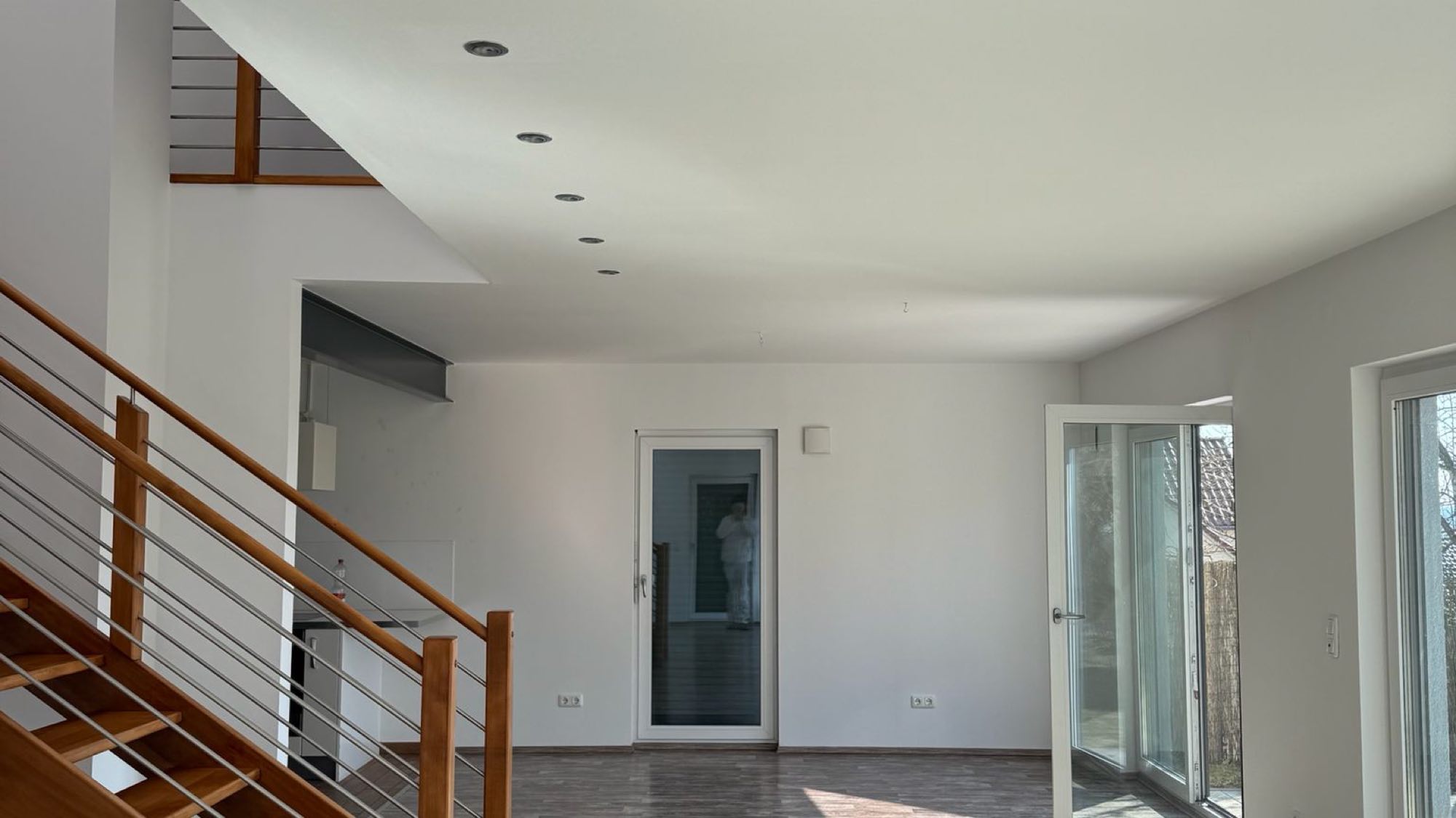 Heller Wohnbereich mit weißen Wänden, Holztreppe und großer Fensterfront nach der Renovierung