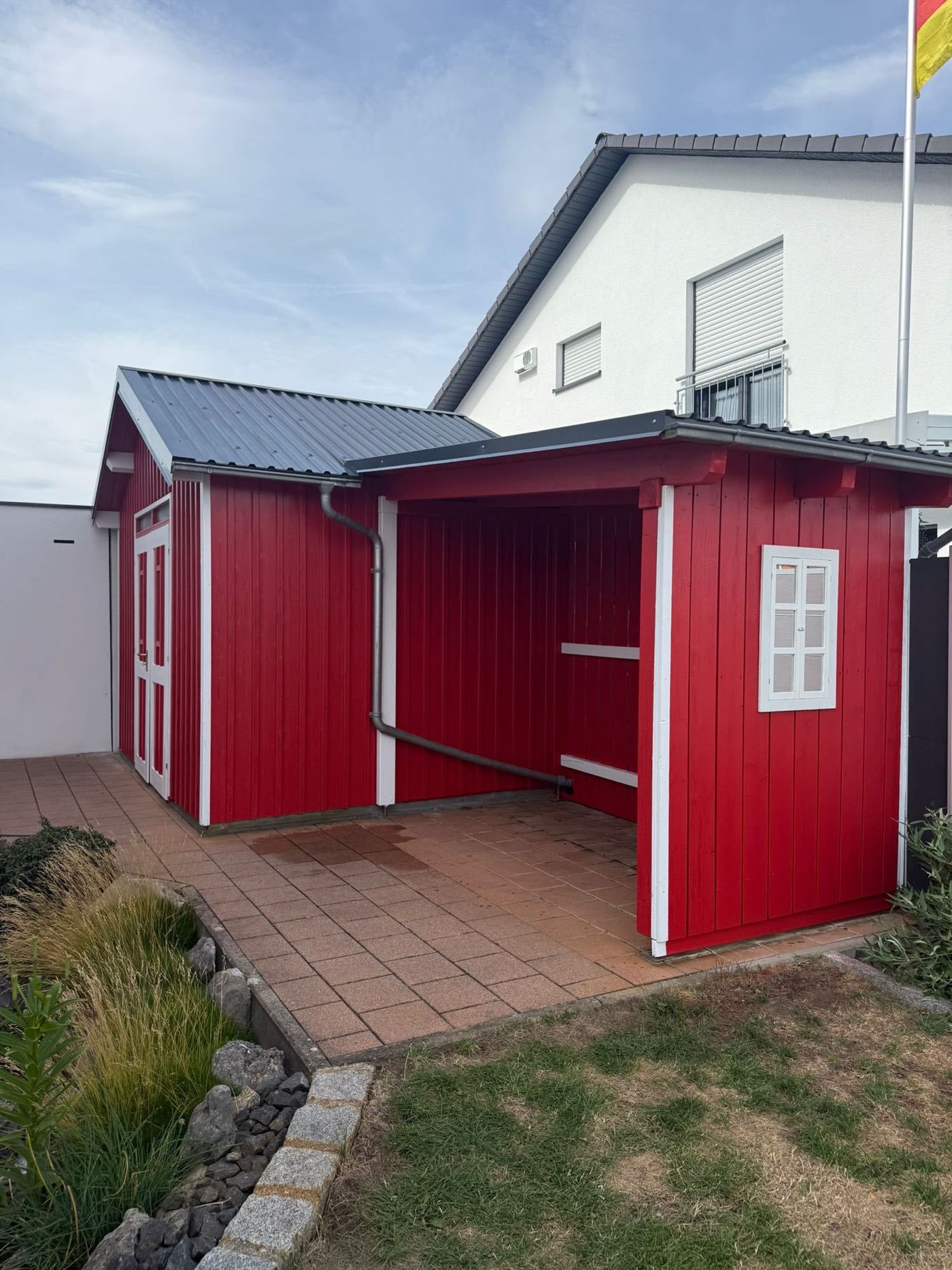 Gartenhaus aus Holz nach dem Neuanstrich in Rot mit weißen Zierleisten