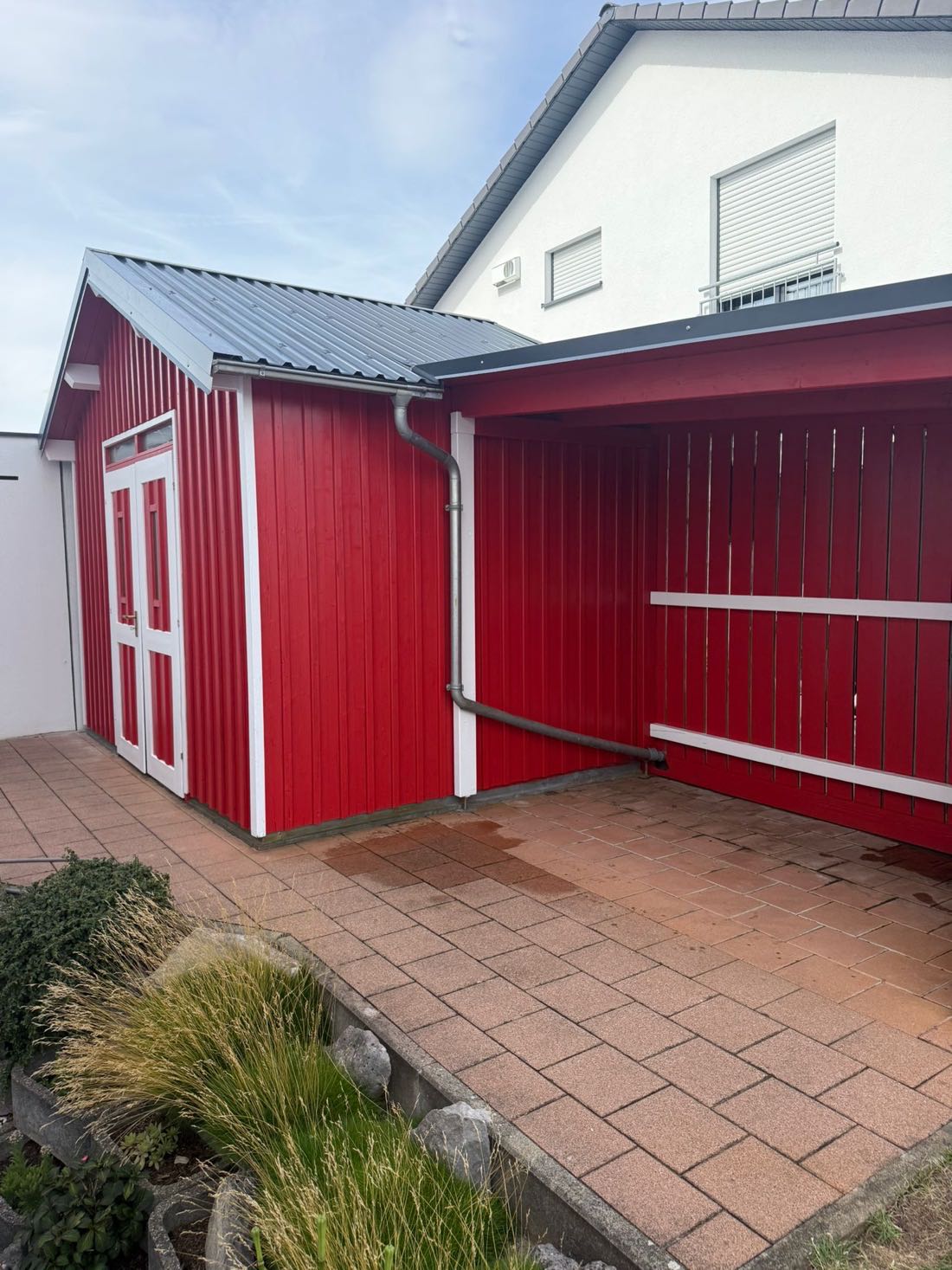 Roter Holzunterstand mit weißen Kanten und Metalldach neben dem Wohnhaus