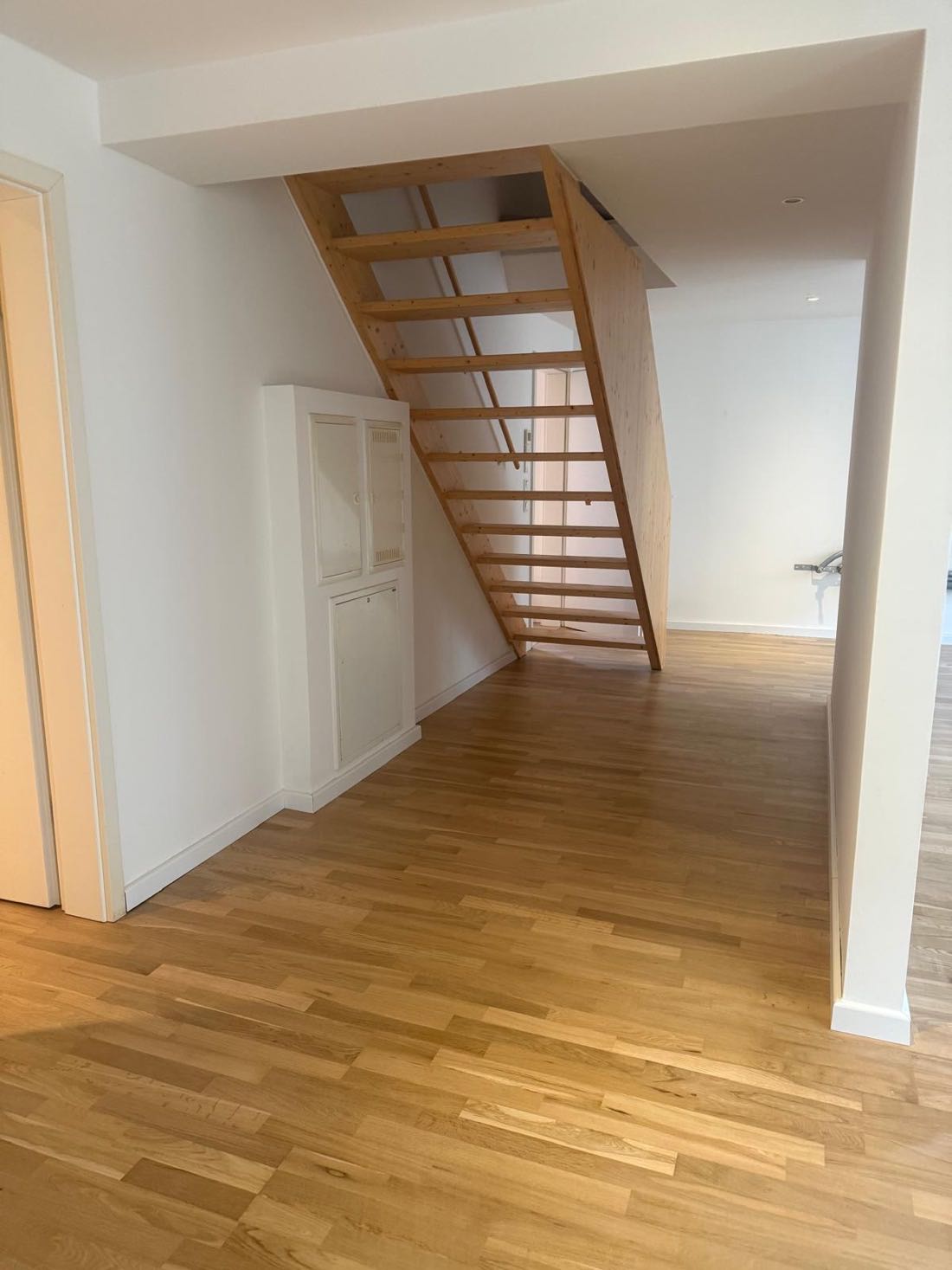 Flur mit offener Holztreppe, weißen Wänden und Eichenboden
