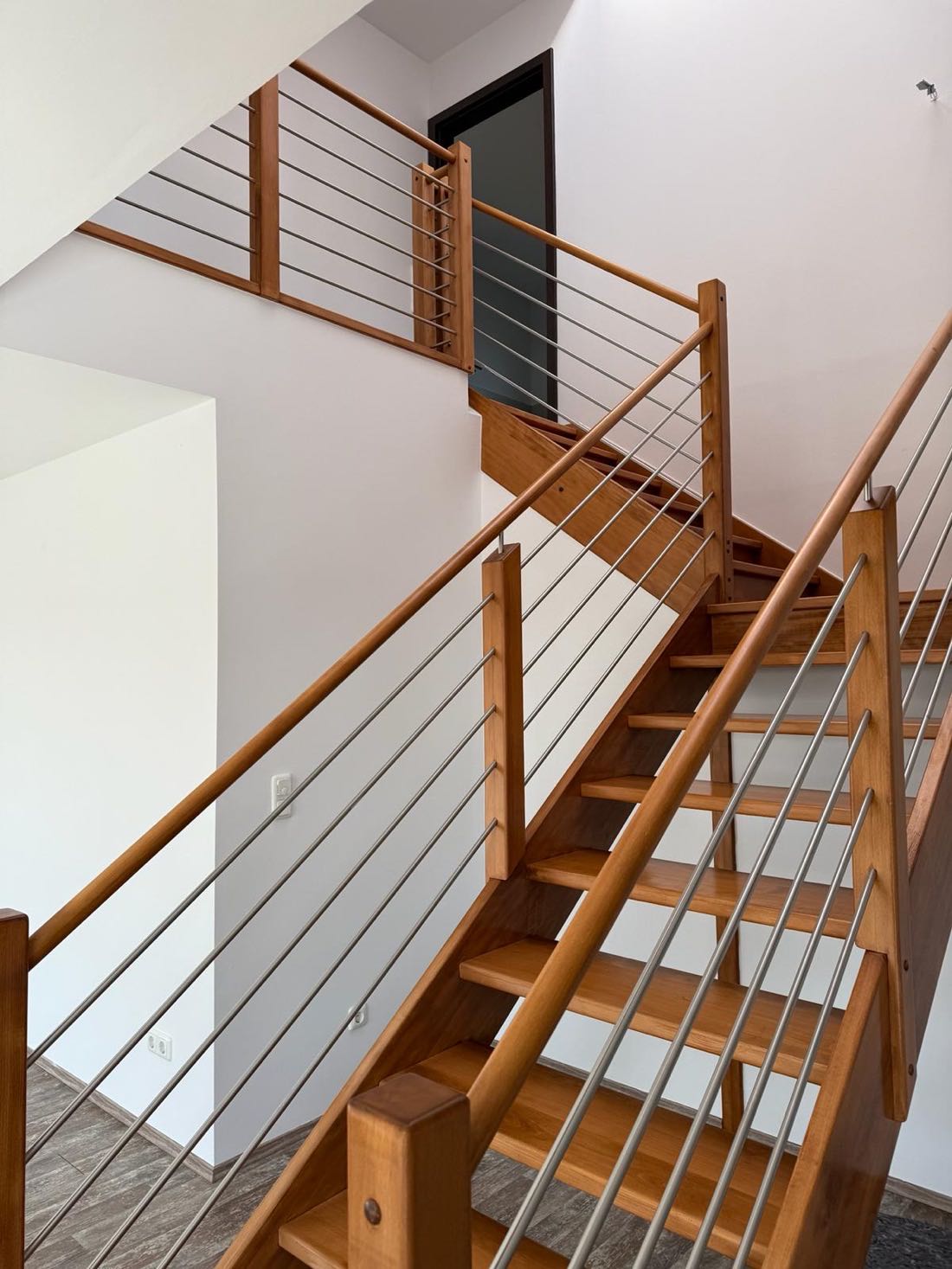 Treppe mit Holzgeländer und Edelstahlstreben vor hell gestrichenen Wandflächen