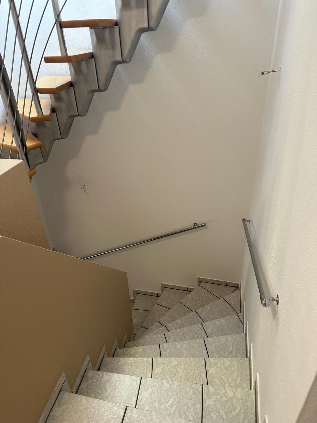 Treppenhaus mit sandfarbener Wandfläche, hellem Handlauf und Steinstufen