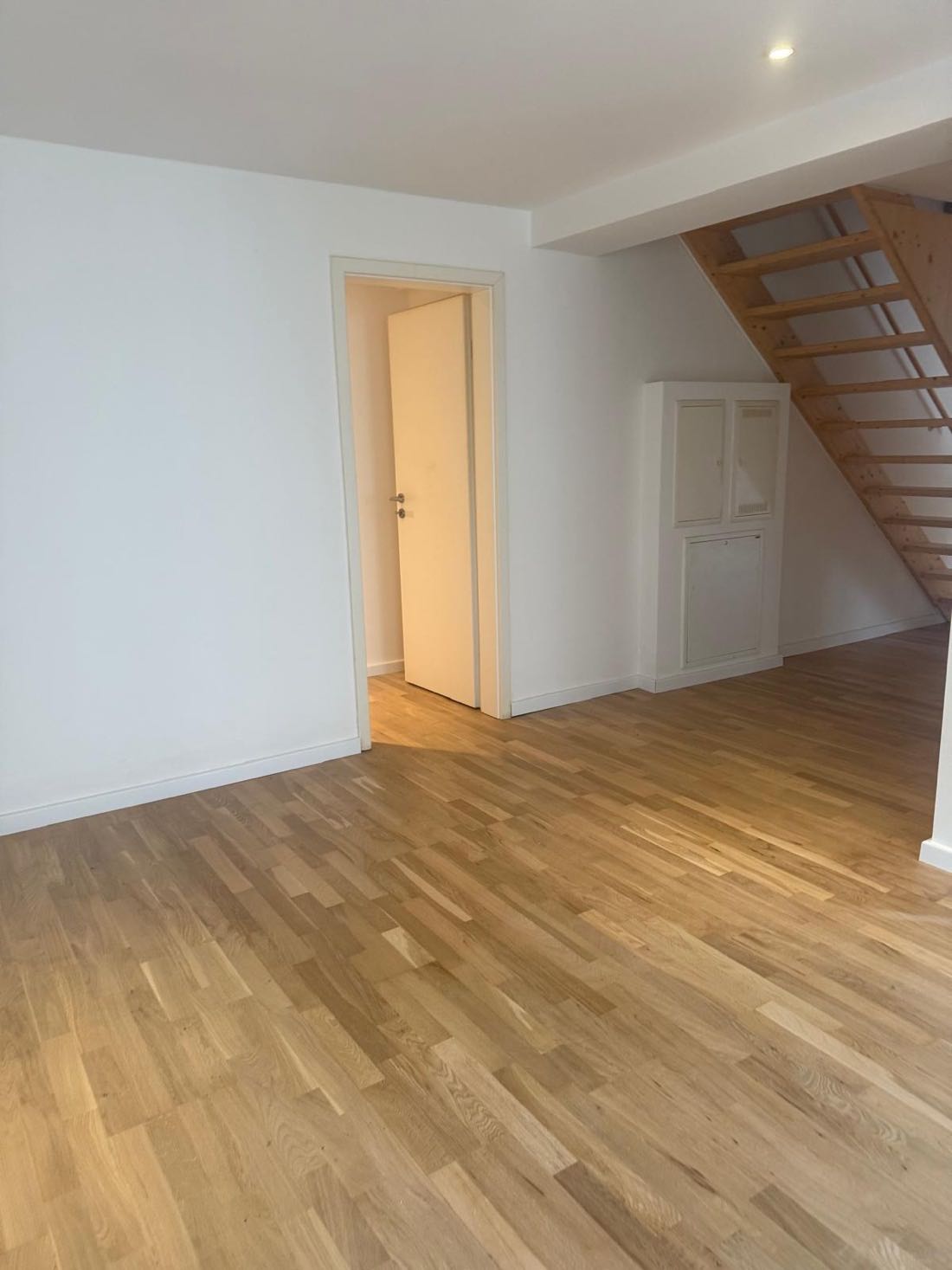 Wohnraum mit Treppenaufgang, weißen Wänden und Eichenboden