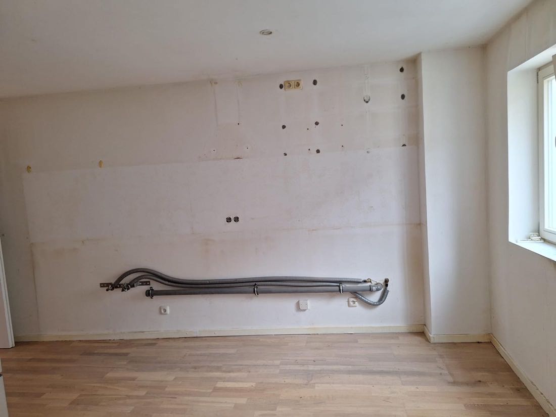 Wandfläche im Rohzustand mit sichtbaren Leitungen und Anschlüssen vor der Renovierung