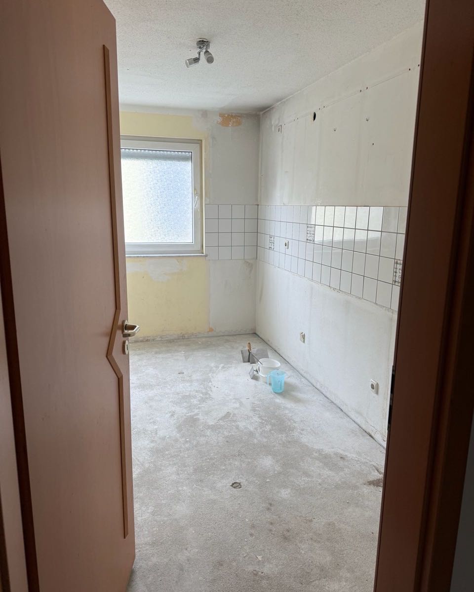 Küche im Rohzustand mit altem Fliesenspiegel und blankem Estrich